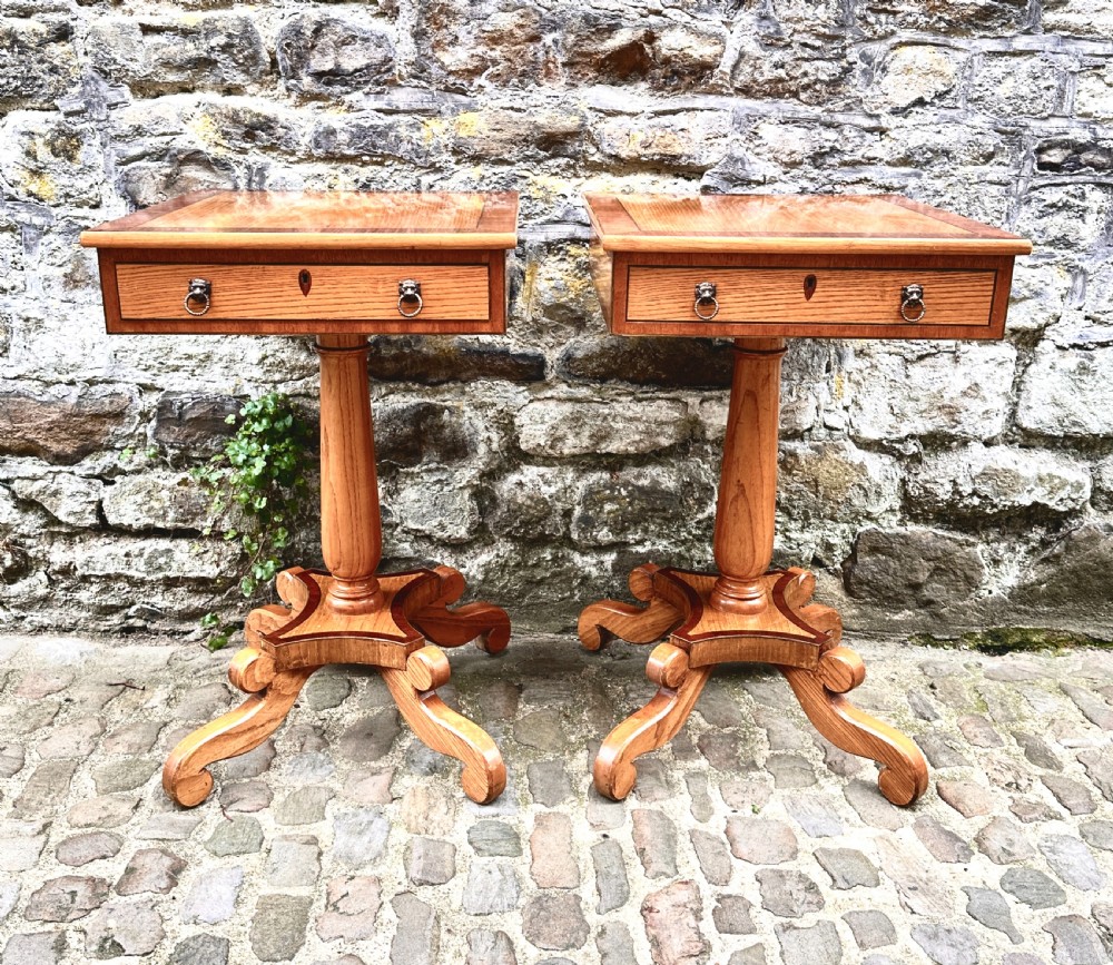 A pair of early 20th century ash pedestal side tables featuring single drawers with brass lion mask ring handles and quadruped scrolled bases.