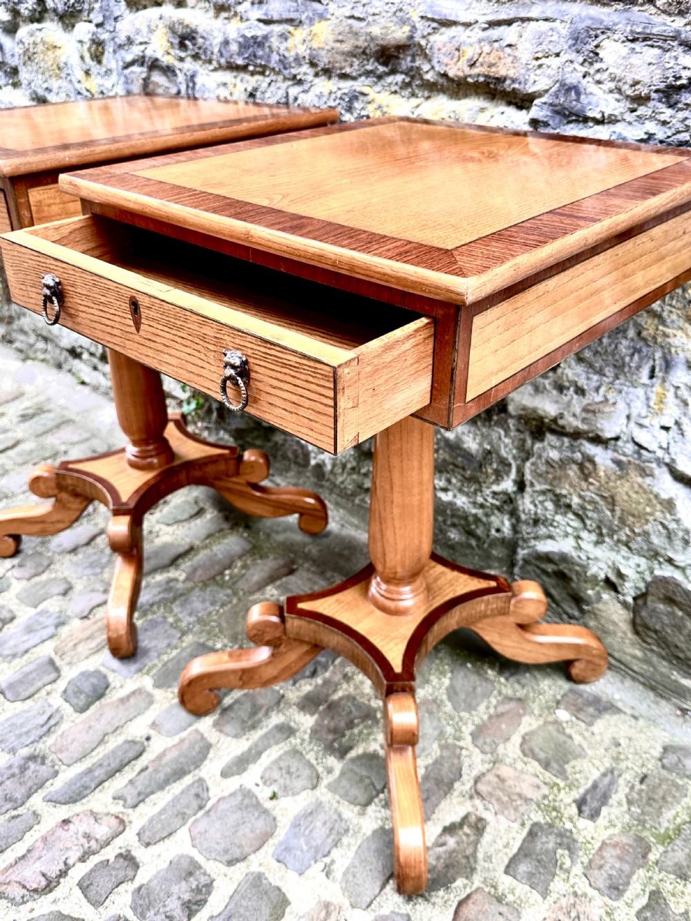 A pair of early 20th century ash pedestal side tables featuring single drawers with brass lion mask ring handles and quadruped scrolled bases. View IV
