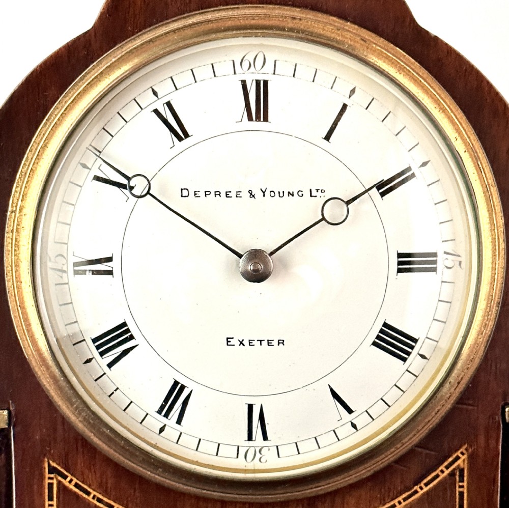 A late Victorian mahogany mantel clock featuring a lancet arch top, brass side pillars, string inlay, brass bracket feet, and a white enamel dial with Roman numerals. View II