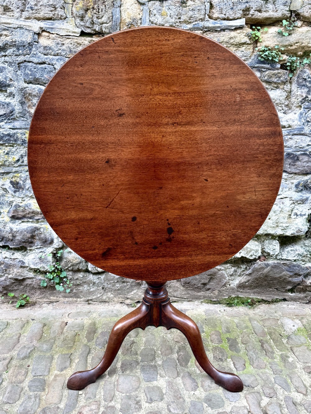 An 18th-century George III mahogany tripod table with a circular tilt top surface, turned column pedestal, and three cabriole legs.