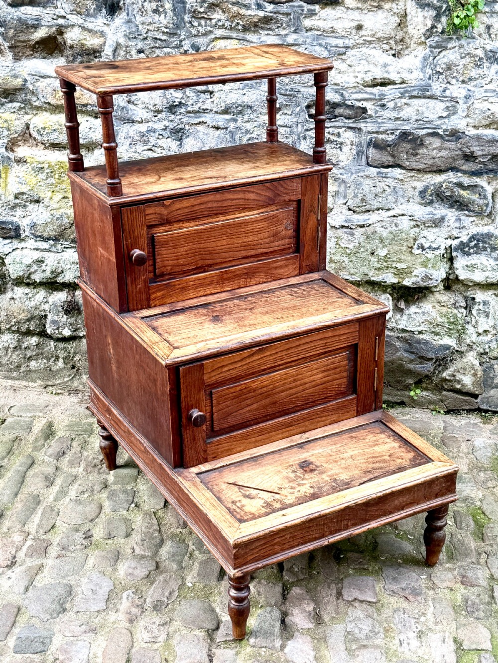 A flight of late Victorian oak library steps featuring three tiers, built-in cupboard doors, and turned support legs.