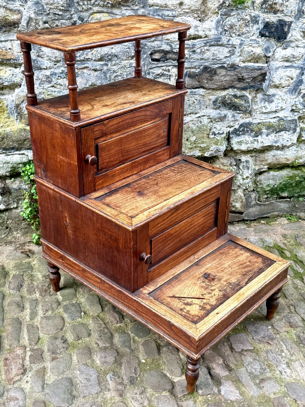 A flight of late Victorian oak library steps featuring three tiers, built-in cupboard doors, and turned support legs. View II