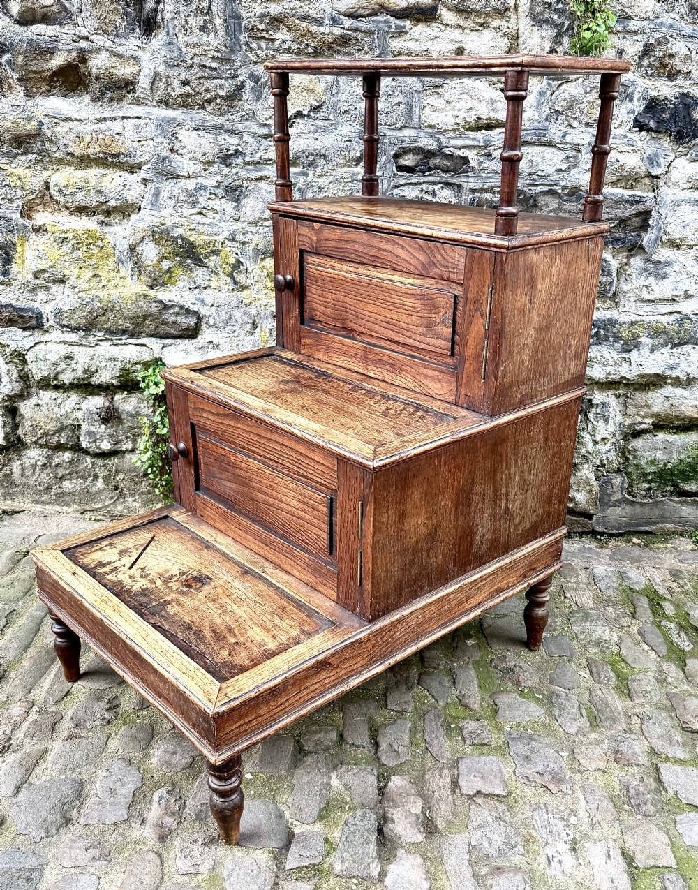 A flight of late Victorian oak library steps featuring three tiers, built-in cupboard doors, and turned support legs. View VI
