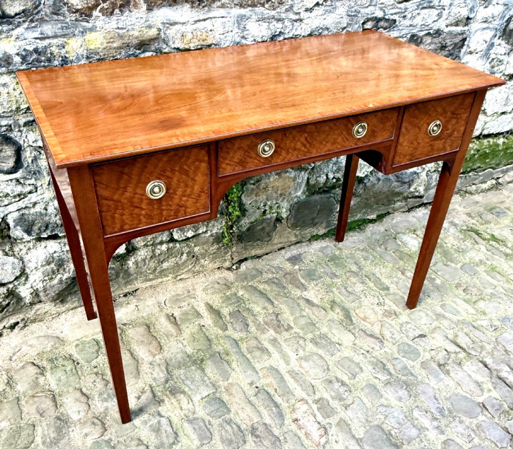 A Sheraton Revival mahogany writing table featuring a rectangular top, three drawers with brass ring drop handles, and slim tapered square legs. View II