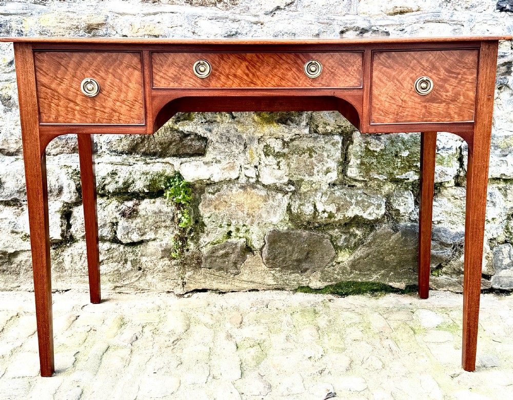 A Sheraton Revival mahogany writing table featuring a rectangular top, three drawers with brass ring drop handles, and slim tapered square legs. View IV