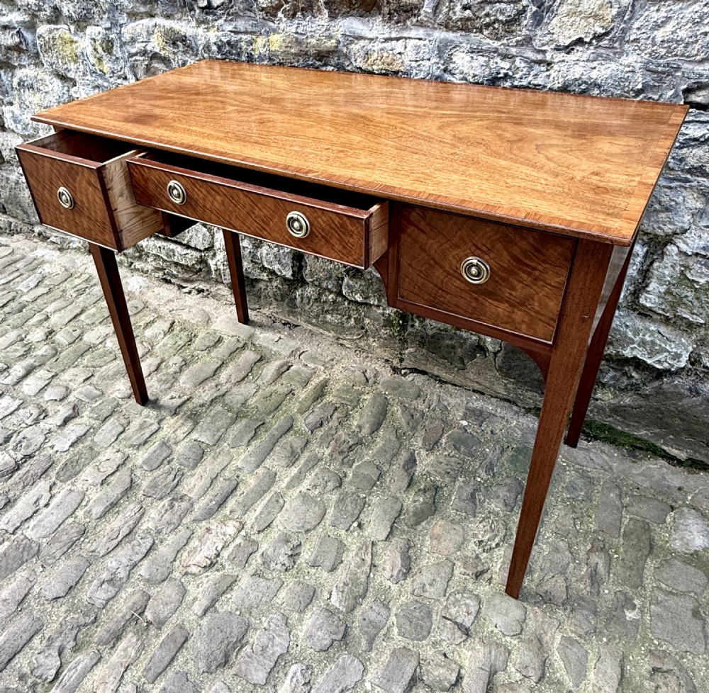 A Sheraton Revival mahogany writing table featuring a rectangular top, three drawers with brass ring drop handles, and slim tapered square legs. View V