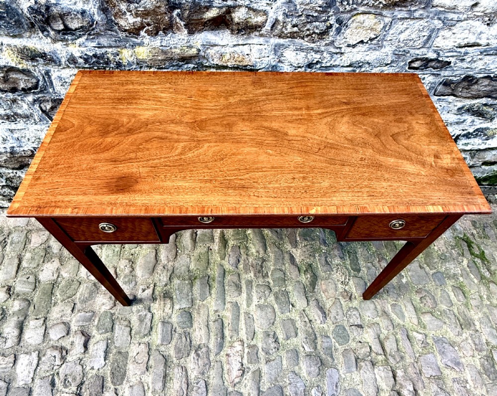 A Sheraton Revival mahogany writing table featuring a rectangular top, three drawers with brass ring drop handles, and slim tapered square legs. View VI