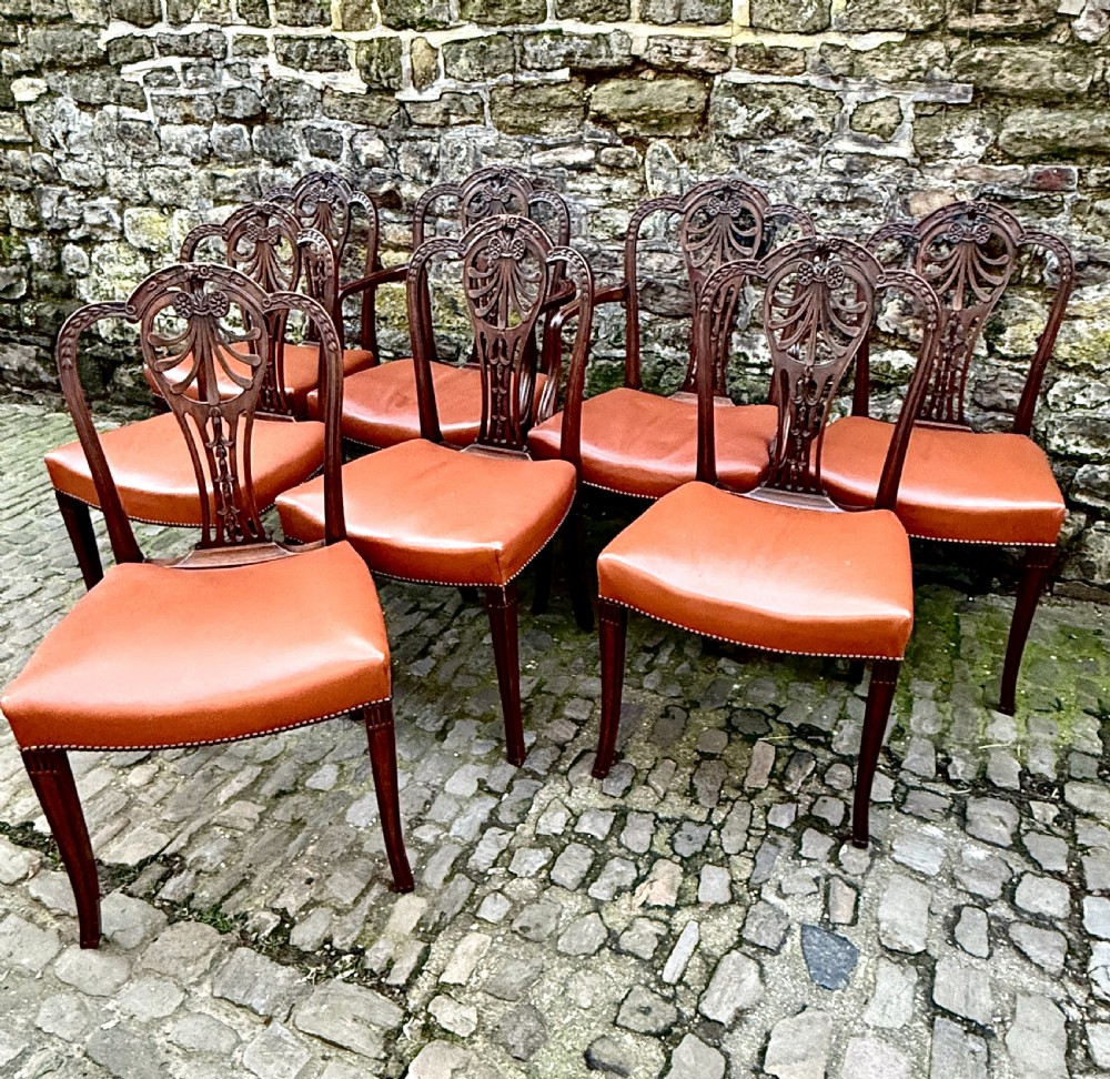 A set of eight carved mahogany dining chairs featuring openwork shield backs and terracotta leather seats secured with brass studs. View II
