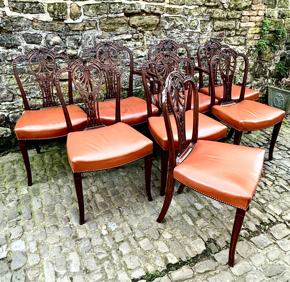 A set of eight carved mahogany dining chairs featuring openwork shield backs and terracotta leather seats secured with brass studs. View III