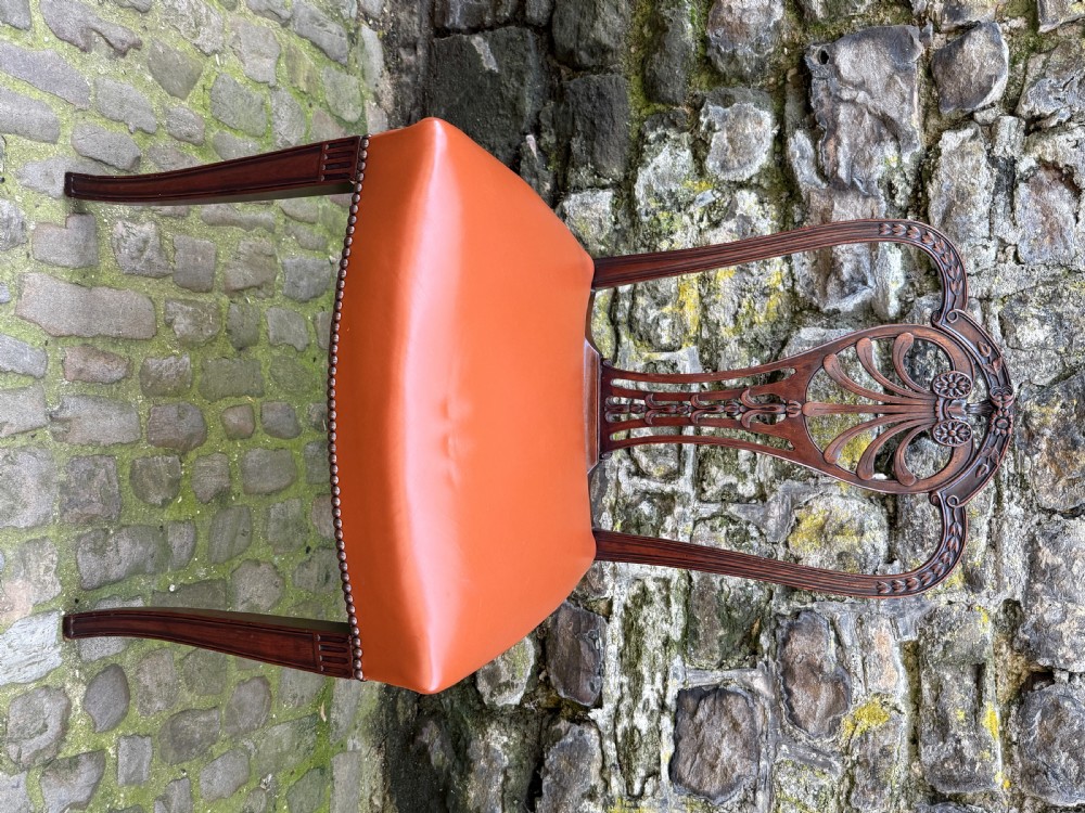 A set of eight carved mahogany dining chairs featuring openwork shield backs and terracotta leather seats secured with brass studs. View V