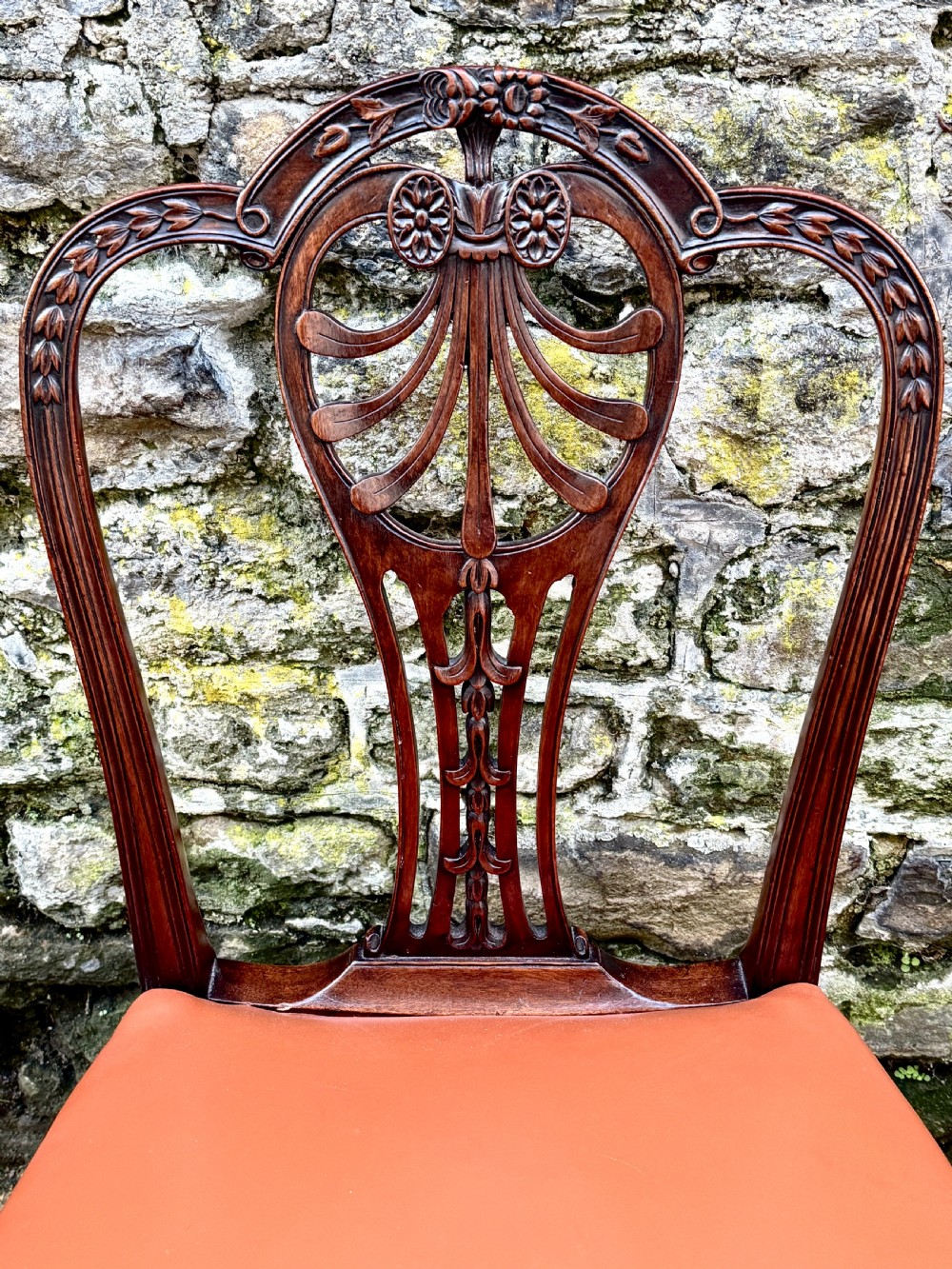 A set of eight carved mahogany dining chairs featuring openwork shield backs and terracotta leather seats secured with brass studs. View VI