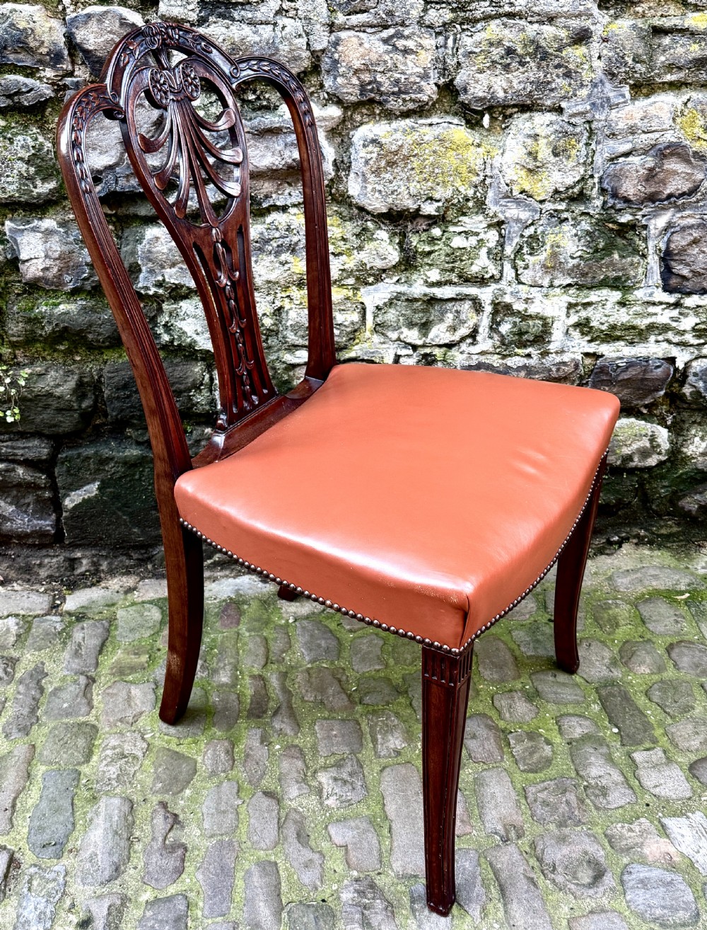 A set of eight carved mahogany dining chairs featuring openwork shield backs and terracotta leather seats secured with brass studs. View VII