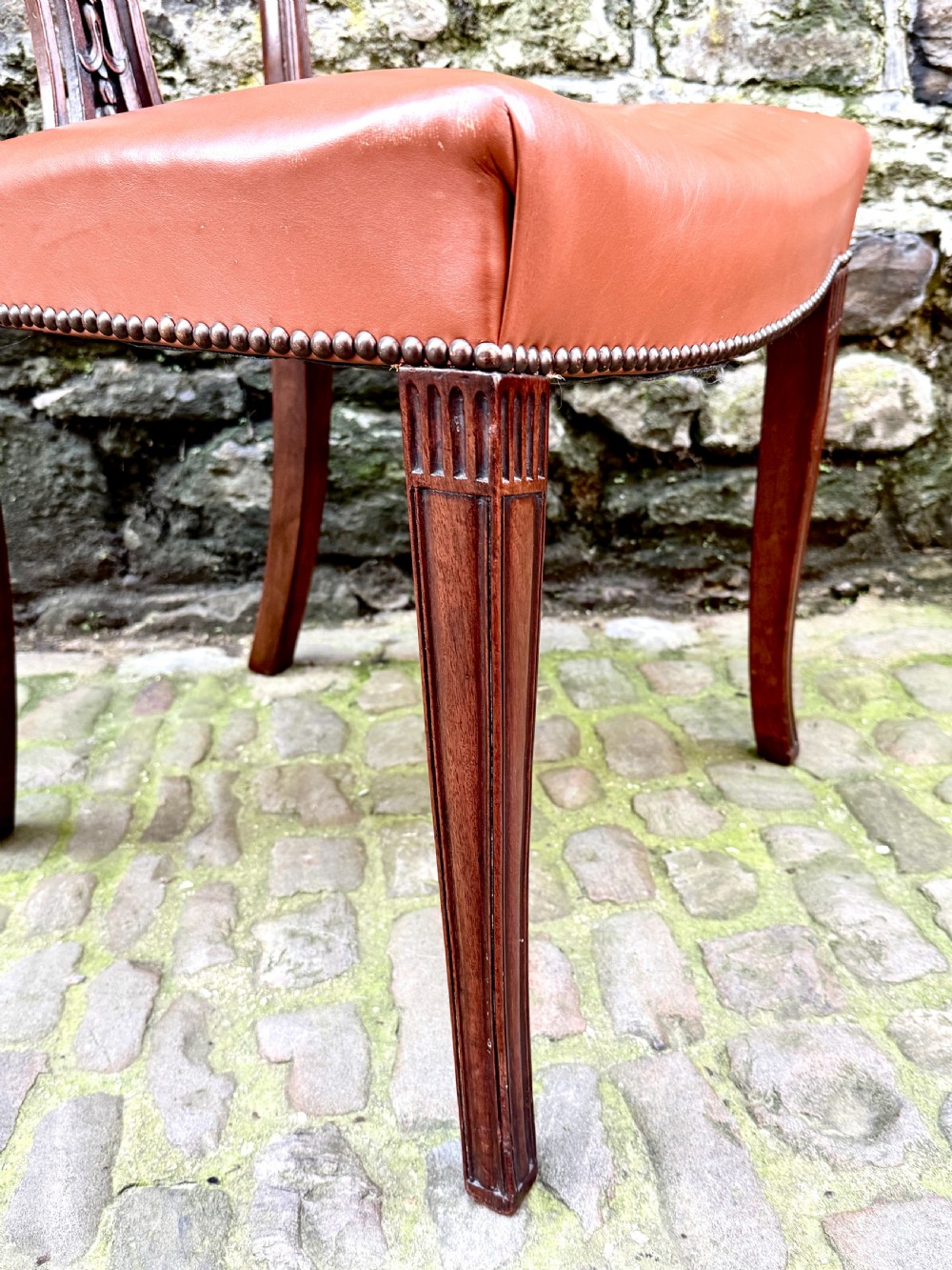 A set of eight carved mahogany dining chairs featuring openwork shield backs and terracotta leather seats secured with brass studs. View VIII