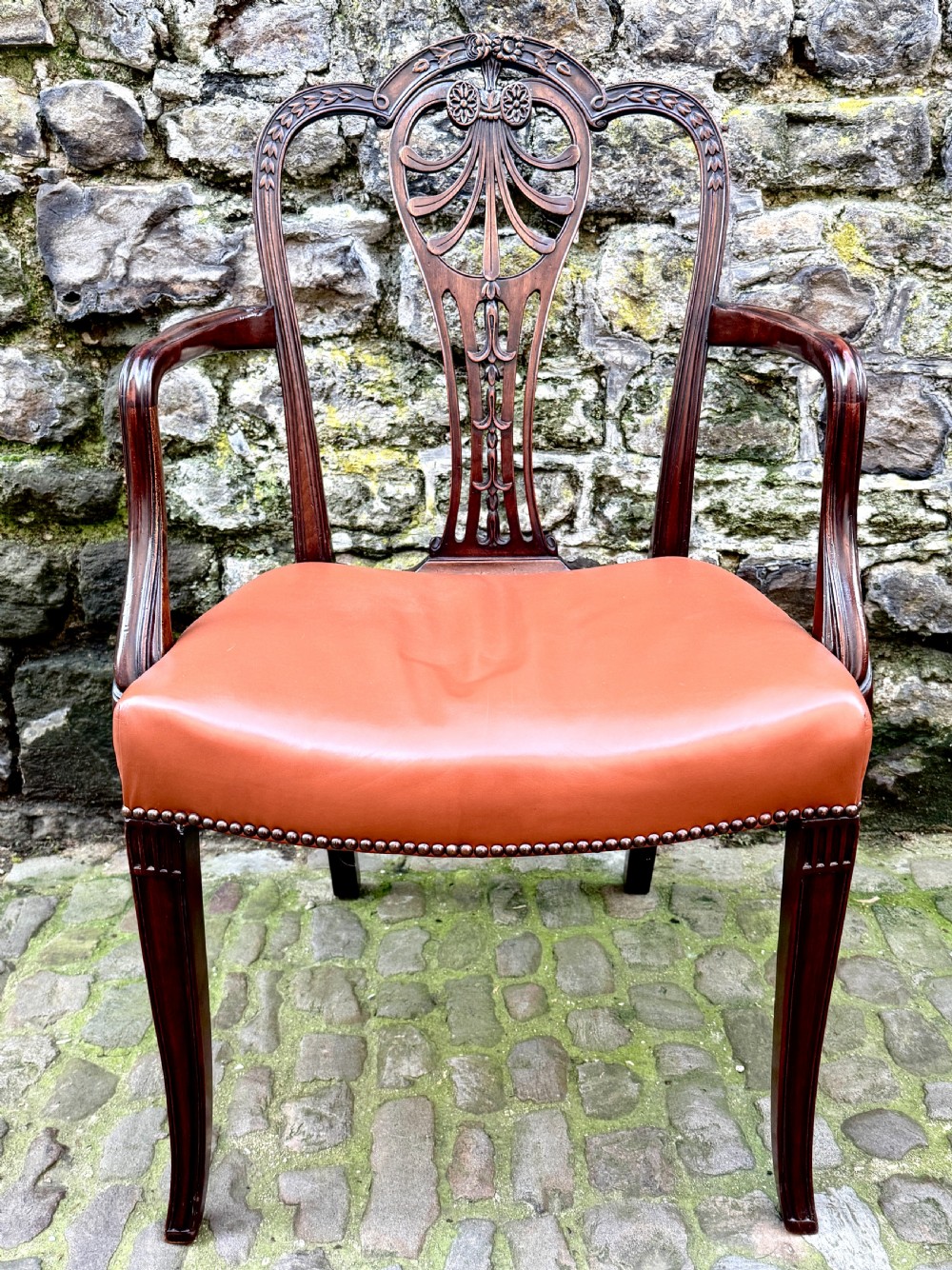 A set of eight carved mahogany dining chairs featuring openwork shield backs and terracotta leather seats secured with brass studs. View X