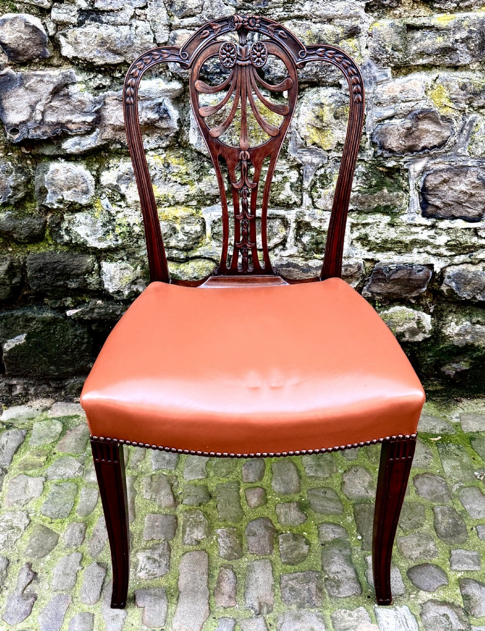 A set of eight carved mahogany dining chairs featuring openwork shield backs and terracotta leather seats secured with brass studs. View XII