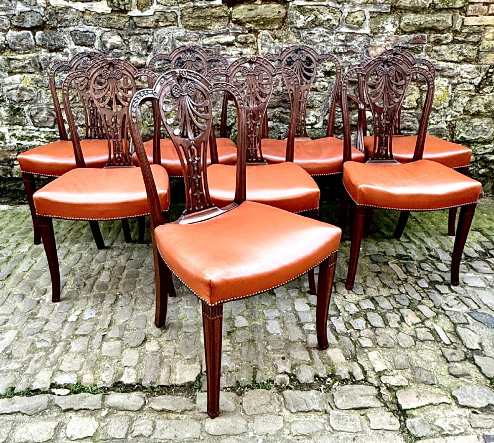 A set of eight carved mahogany dining chairs featuring openwork shield backs and terracotta leather seats secured with brass studs. View XIII