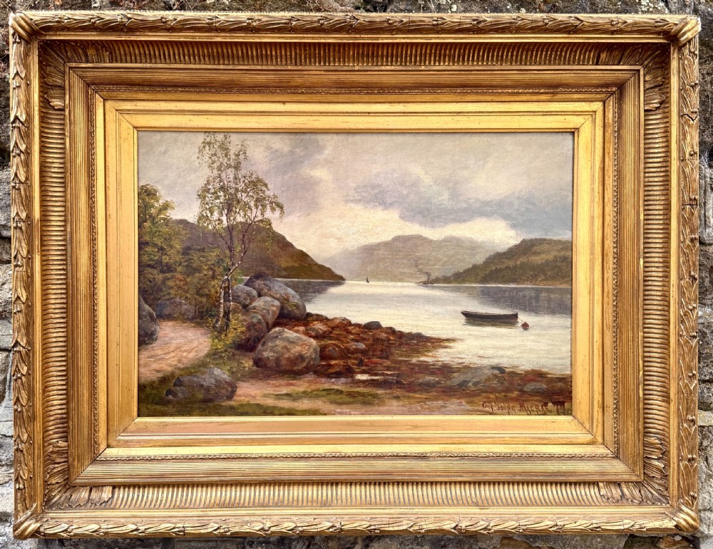 A Victorian oil painting depicting a calm Scottish loch with trees, rocky shorelines, and distant hills set inside a heavy moulded gilt wood frame.