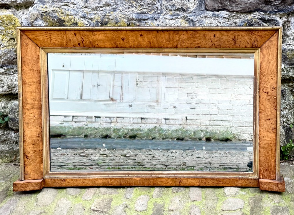 A rectangular early 19th-century Regency overmantel mirror framed in figured burl wood veneer with an inner gilt slip border and corner plinth feet.