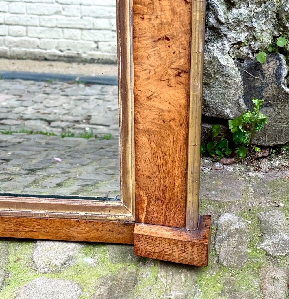 A rectangular early 19th-century Regency overmantel mirror framed in figured burl wood veneer with an inner gilt slip border and corner plinth feet. View II