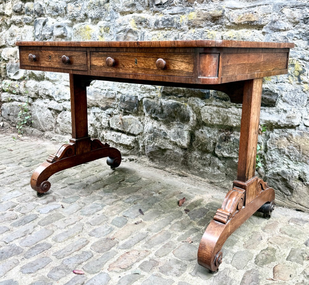 A George IV rosewood library table with a figured timber top, frieze drawers, turned handles, and carved scrolled feet. View III