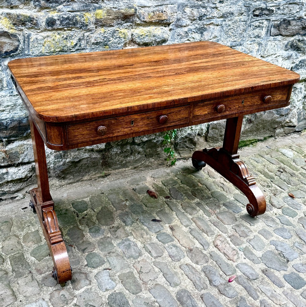A George IV rosewood library table with a figured timber top, frieze drawers, turned handles, and carved scrolled feet. View VI