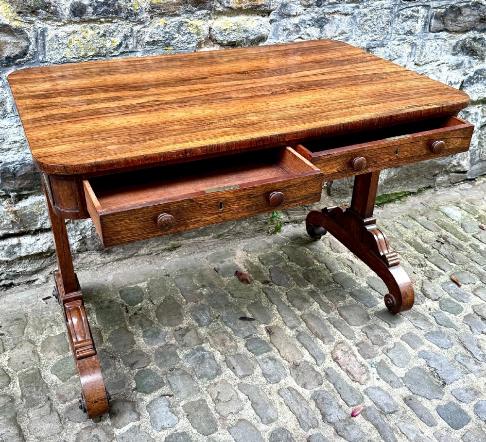 A George IV rosewood library table with a figured timber top, frieze drawers, turned handles, and carved scrolled feet. View VIII
