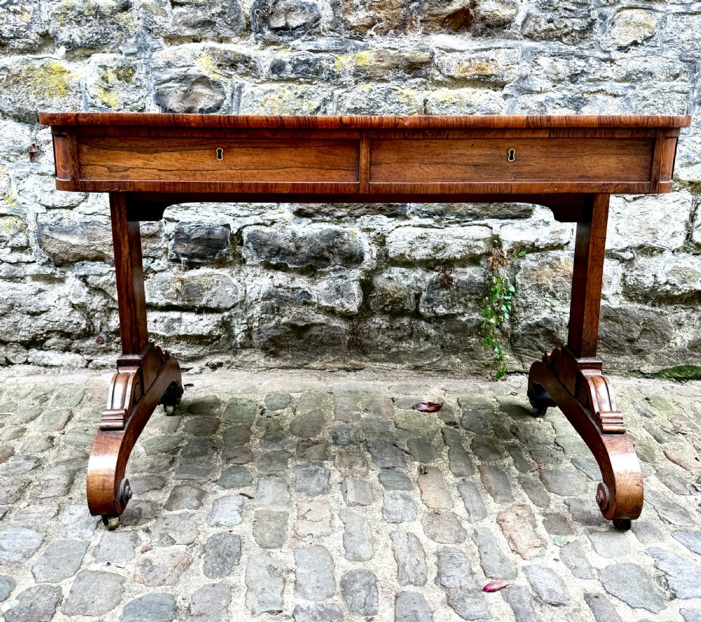 A George IV rosewood library table with a figured timber top, frieze drawers, turned handles, and carved scrolled feet. View IX