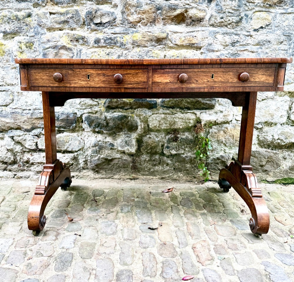A George IV rosewood library table with a figured timber top, frieze drawers, turned handles, and carved scrolled feet. View X