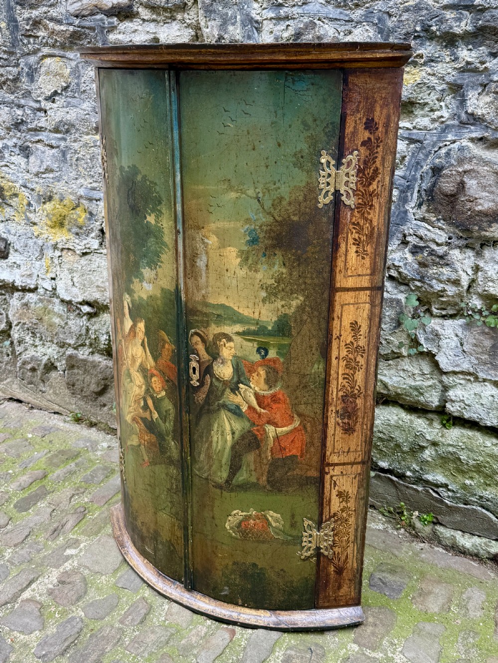 An eighteenth-century George II bowfront corner cupboard featuring two curved doors painted with a green pastoral scene and fitted with pierced brass hinges. View IV