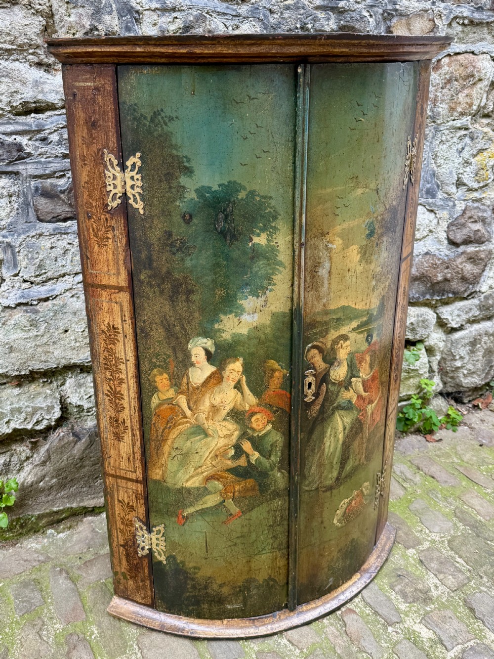 An eighteenth-century George II bowfront corner cupboard featuring two curved doors painted with a green pastoral scene and fitted with pierced brass hinges. View V