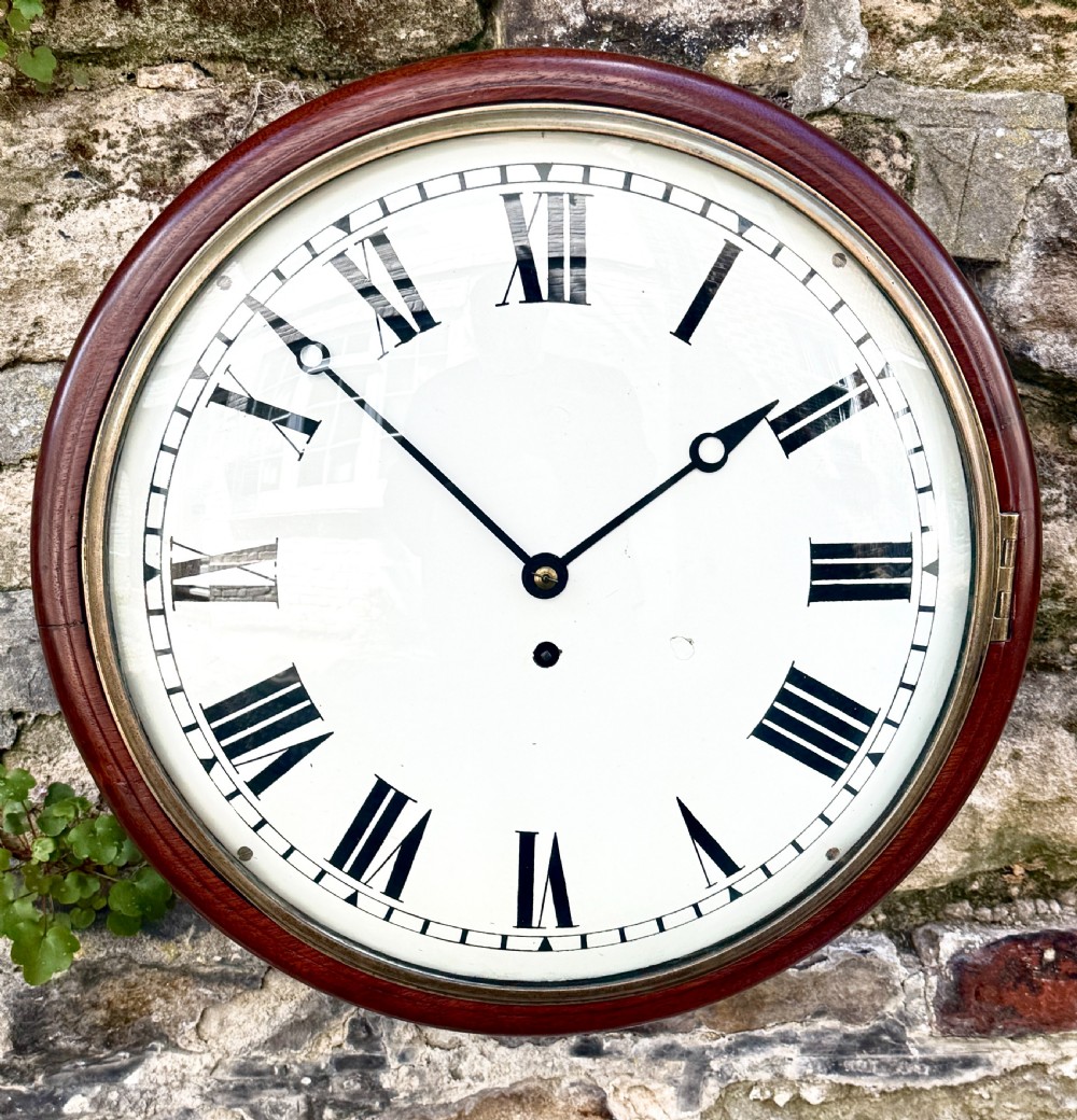 An early nineteenth-century circular English wall clock featuring a dark mahogany surround, brass-rimmed glass face, and a white dial with black Roman numerals.