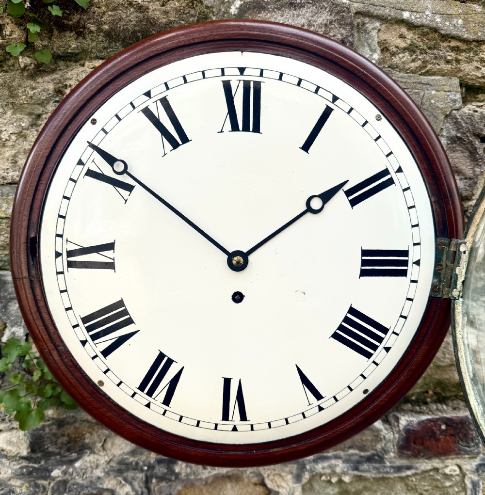 An early nineteenth-century circular English wall clock featuring a dark mahogany surround, brass-rimmed glass face, and a white dial with black Roman numerals. View II