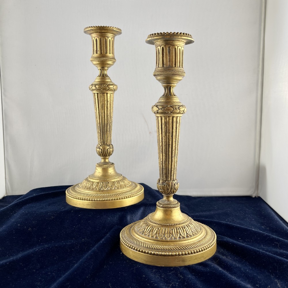 A pair of cast gilt bronze candlesticks featuring tapered fluted stems, acanthus leaf details, and circular beaded bases. View II