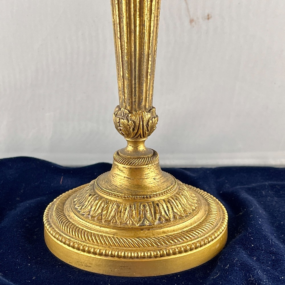 A pair of cast gilt bronze candlesticks featuring tapered fluted stems, acanthus leaf details, and circular beaded bases. View IV