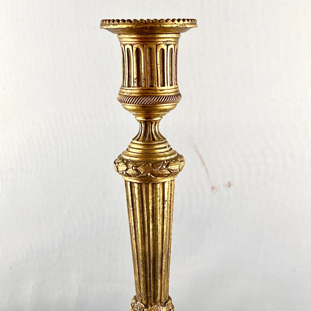 A pair of cast gilt bronze candlesticks featuring tapered fluted stems, acanthus leaf details, and circular beaded bases. View V