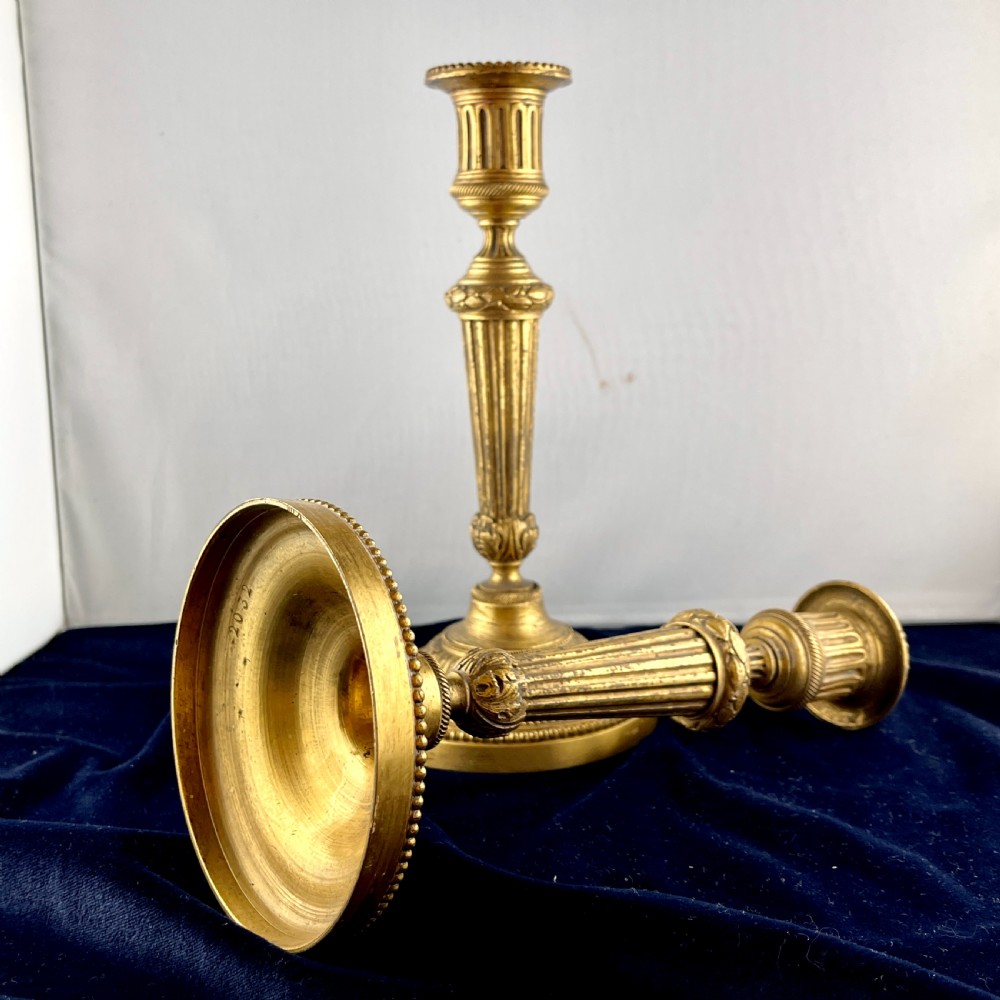 A pair of cast gilt bronze candlesticks featuring tapered fluted stems, acanthus leaf details, and circular beaded bases. View VI