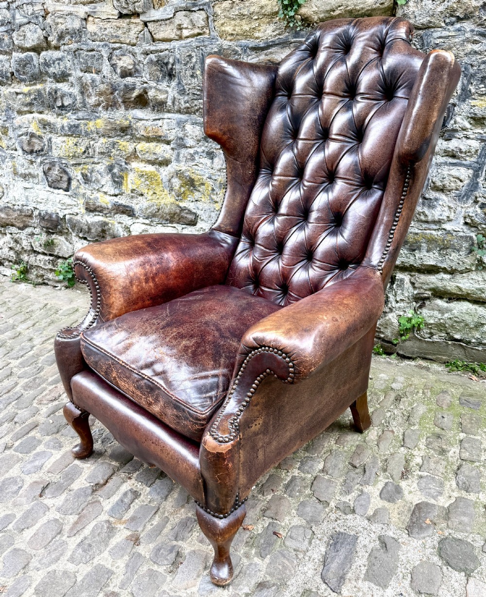 A late Victorian wingback armchair upholstered in deep-buttoned dark brown leather with brass studding details and cabriole front legs. View XI