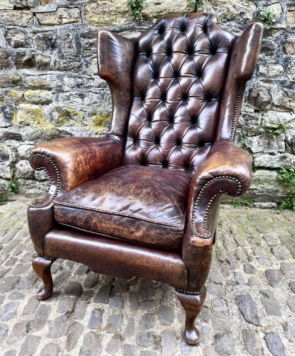 A late Victorian wingback armchair upholstered in deep-buttoned dark brown leather with brass studding details and cabriole front legs.