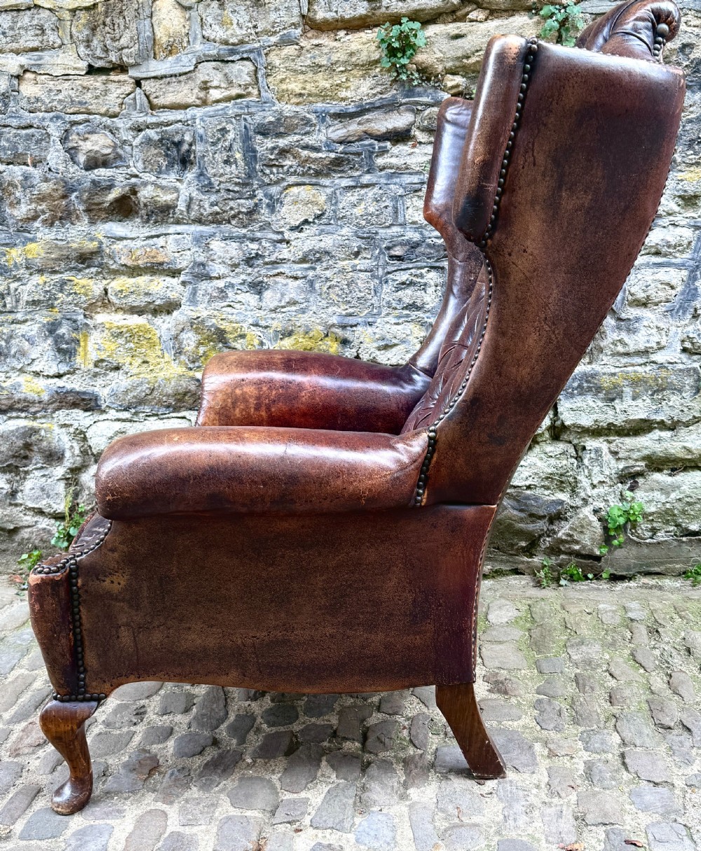 A late Victorian wingback armchair upholstered in deep-buttoned dark brown leather with brass studding details and cabriole front legs. View II
