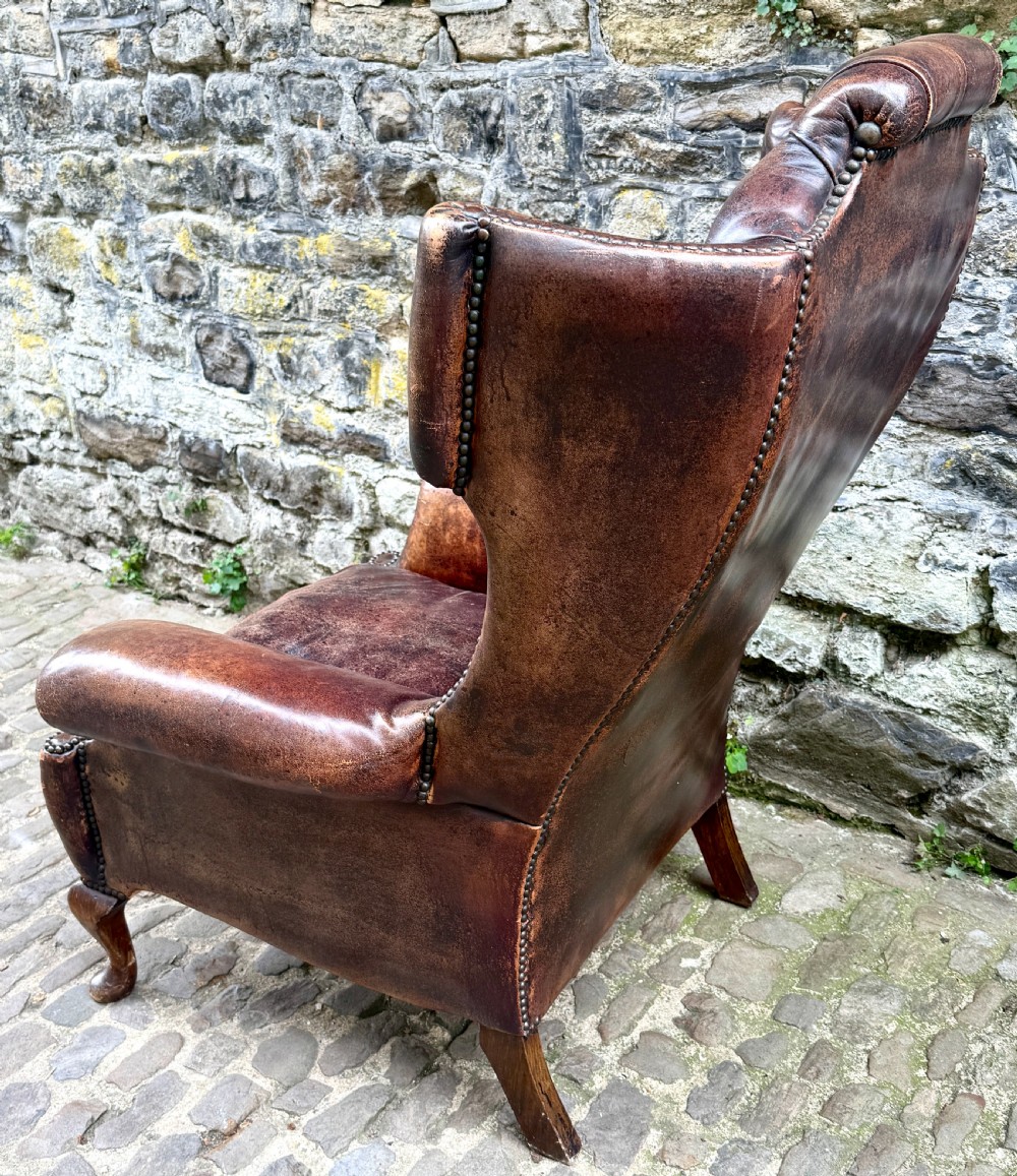 A late Victorian wingback armchair upholstered in deep-buttoned dark brown leather with brass studding details and cabriole front legs. View III