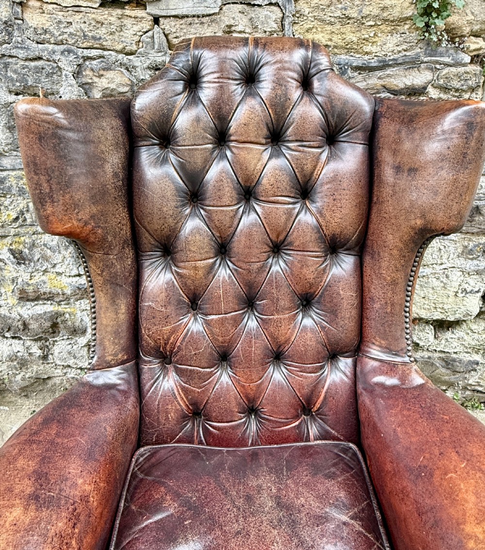A late Victorian wingback armchair upholstered in deep-buttoned dark brown leather with brass studding details and cabriole front legs. View IV