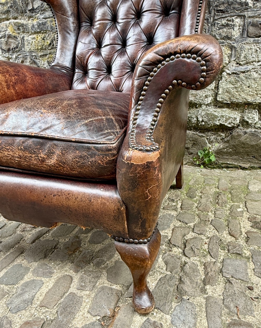 A late Victorian wingback armchair upholstered in deep-buttoned dark brown leather with brass studding details and cabriole front legs. View V
