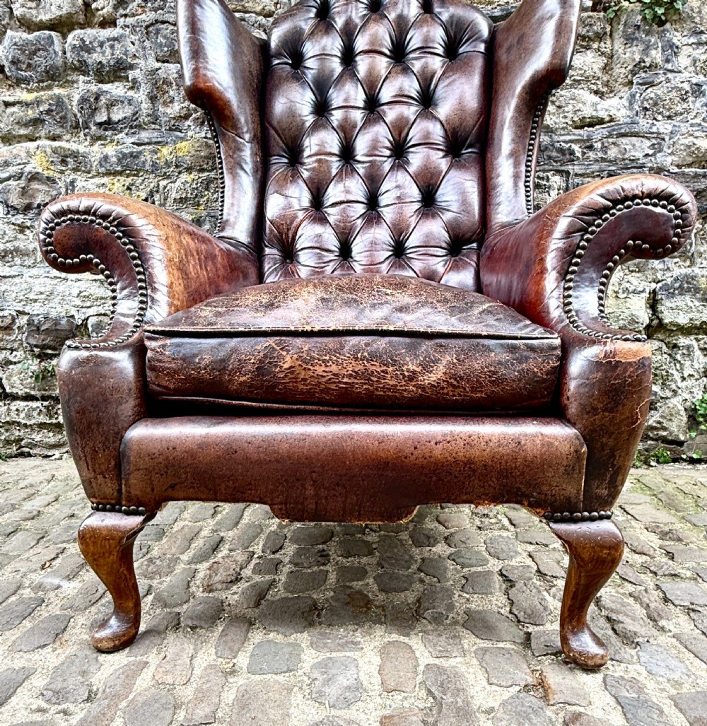 A late Victorian wingback armchair upholstered in deep-buttoned dark brown leather with brass studding details and cabriole front legs. View VI