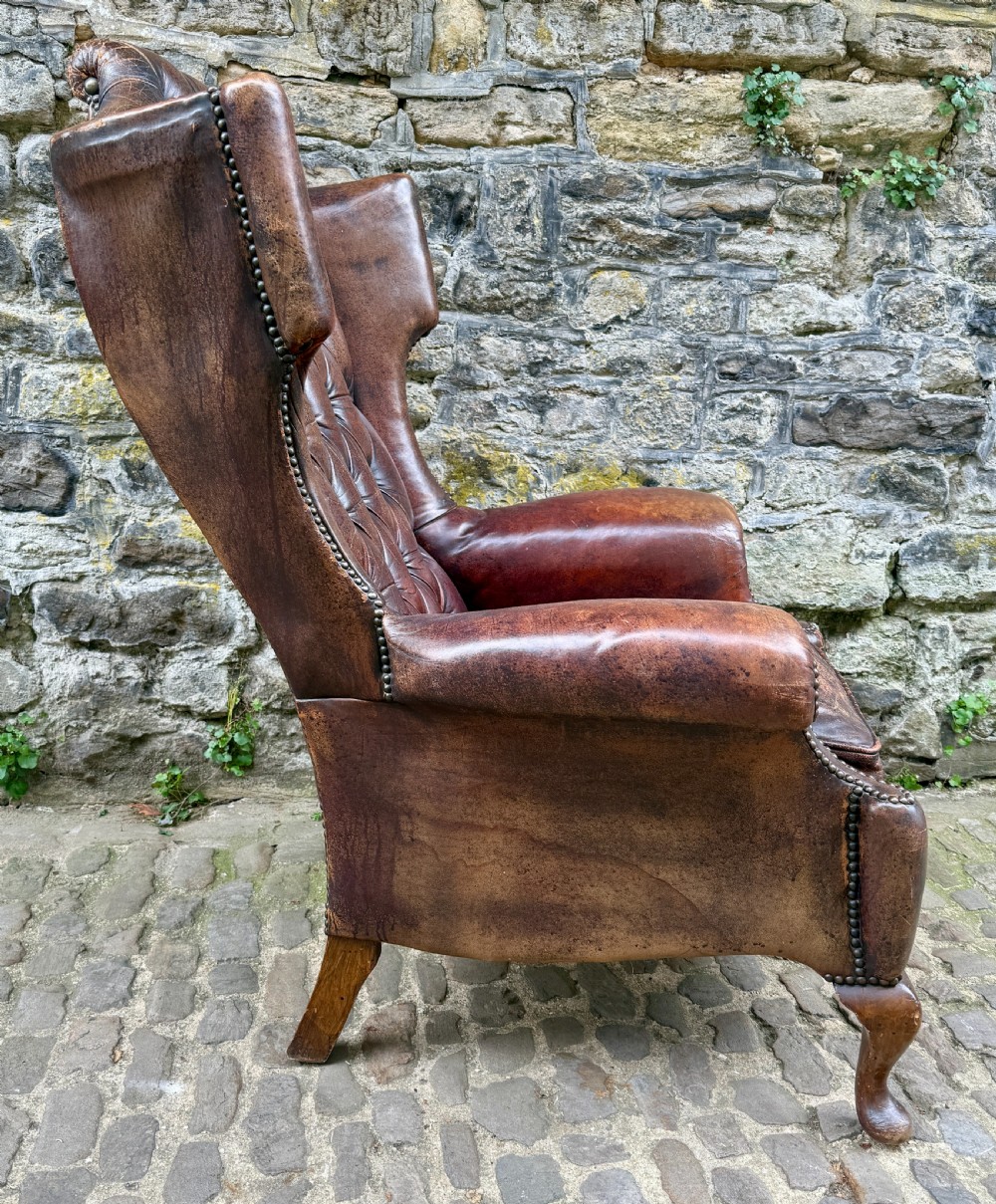 A late Victorian wingback armchair upholstered in deep-buttoned dark brown leather with brass studding details and cabriole front legs. View VII