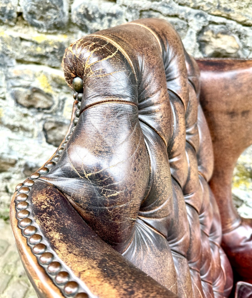 A late Victorian wingback armchair upholstered in deep-buttoned dark brown leather with brass studding details and cabriole front legs. View VIII