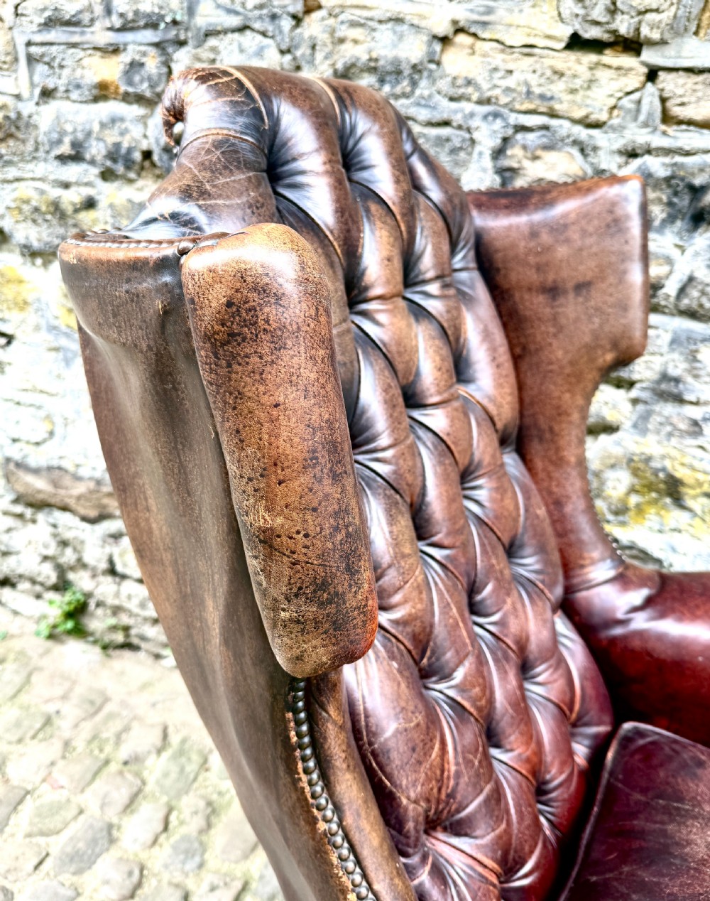A late Victorian wingback armchair upholstered in deep-buttoned dark brown leather with brass studding details and cabriole front legs. View IX