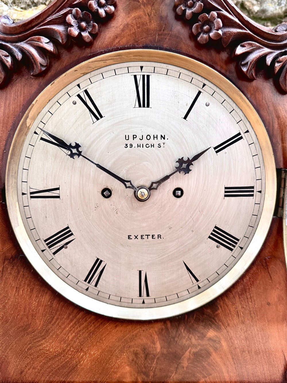 A mid-Victorian mahogany bracket clock featuring a carved scroll case, silvered circular dial with Roman numerals, and an ornate plinth base. View III