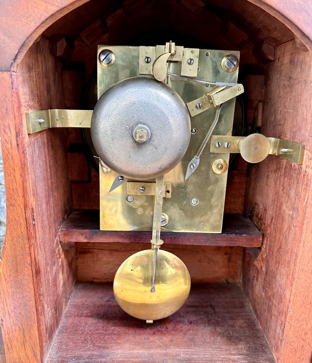A mid-Victorian mahogany bracket clock featuring a carved scroll case, silvered circular dial with Roman numerals, and an ornate plinth base. View V