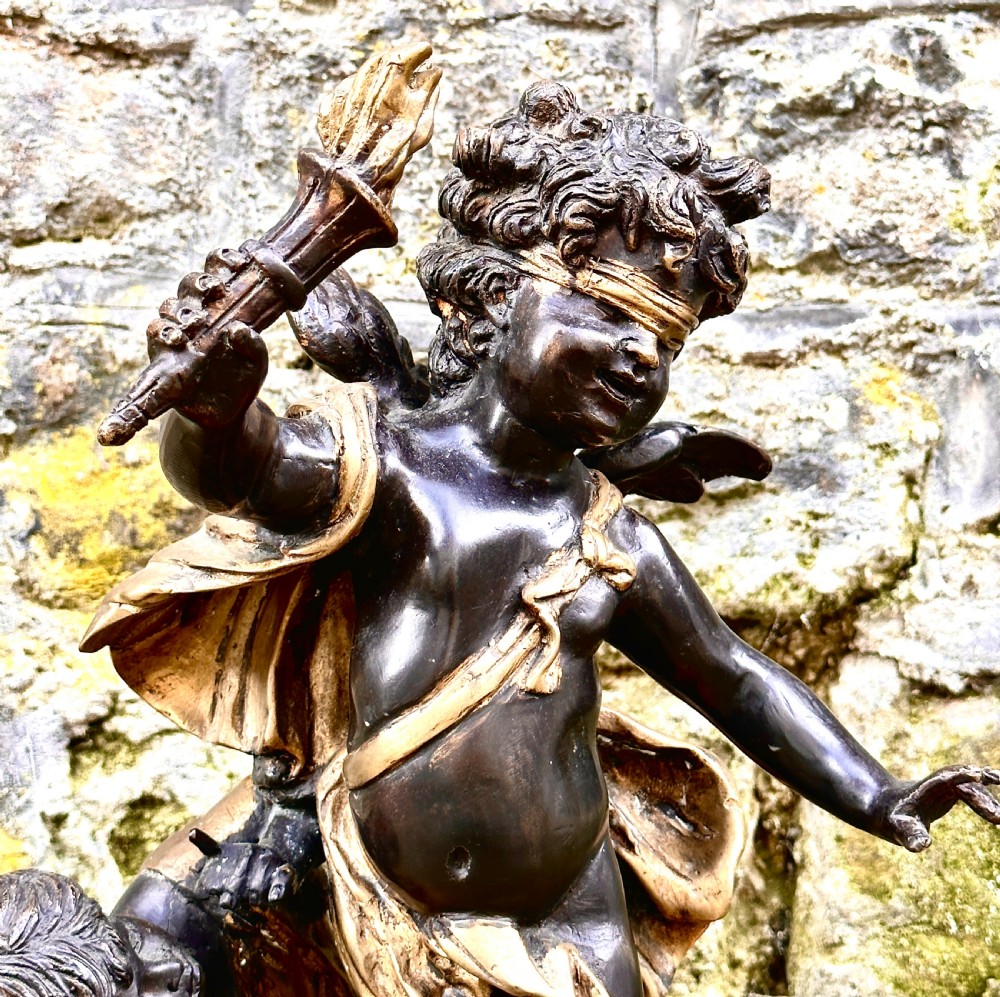 A dark bronze and parcel-gilt French sculpture depicting a blindfolded winged cherub holding a flaming torch, mounted on a round black marble base. View II
