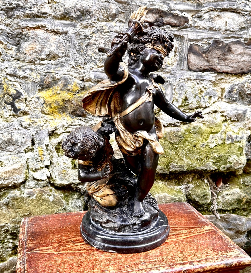 A dark bronze and parcel-gilt French sculpture depicting a blindfolded winged cherub holding a flaming torch, mounted on a round black marble base. View III